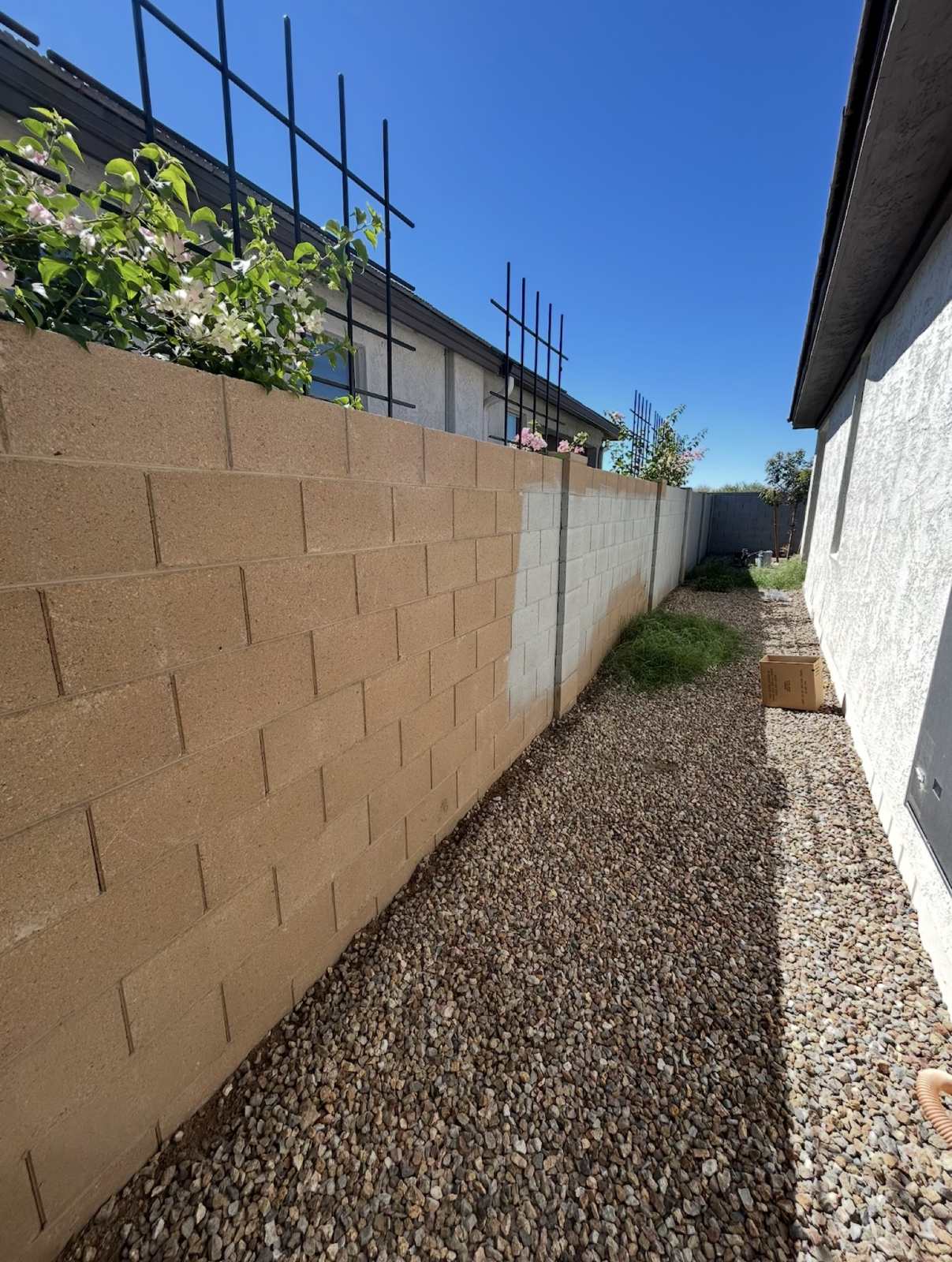 Before: tan concrete block wall along a gravel side yard, partly primed gray at the far end