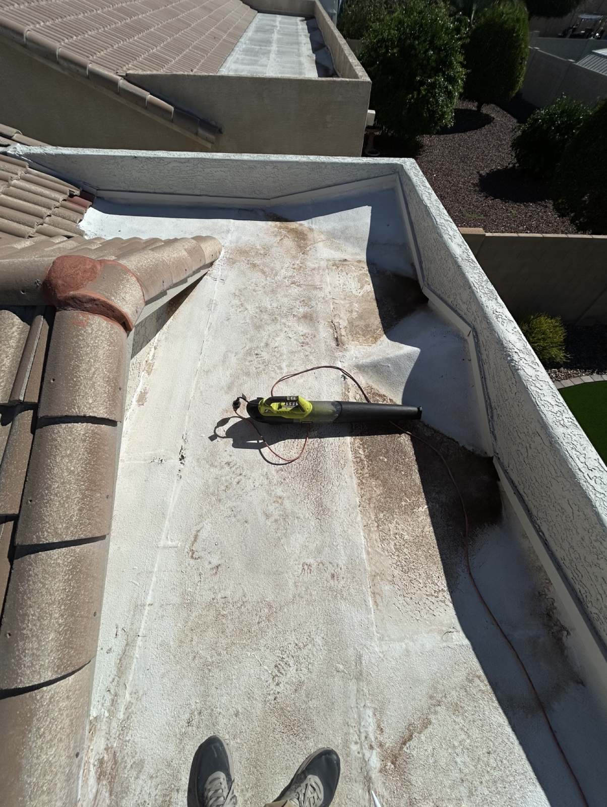 Before: weathered, dirty flat roof section between a tile roof and a stucco parapet wall