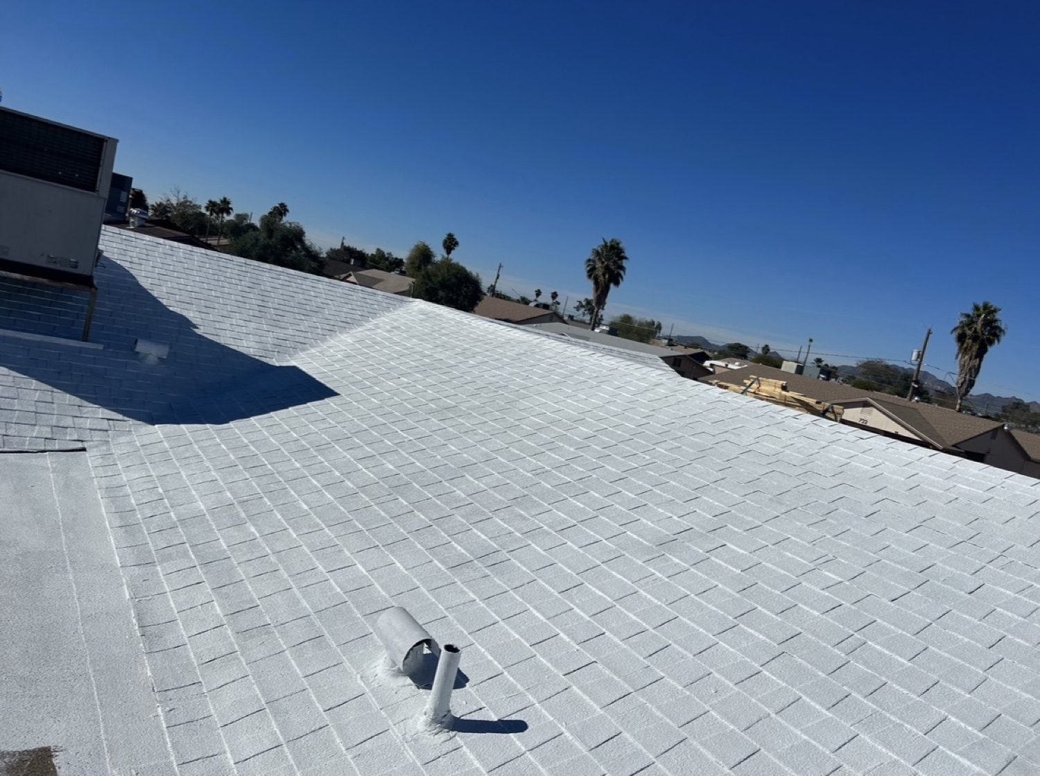 Asphalt shingle roof finished with a white reflective roof coating, vent pipe in the foreground