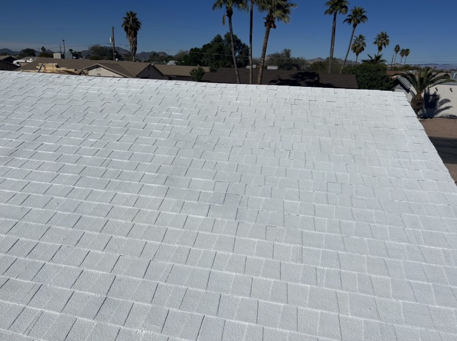 Asphalt shingle roof covered in a white reflective roof coating, with palm trees in the background