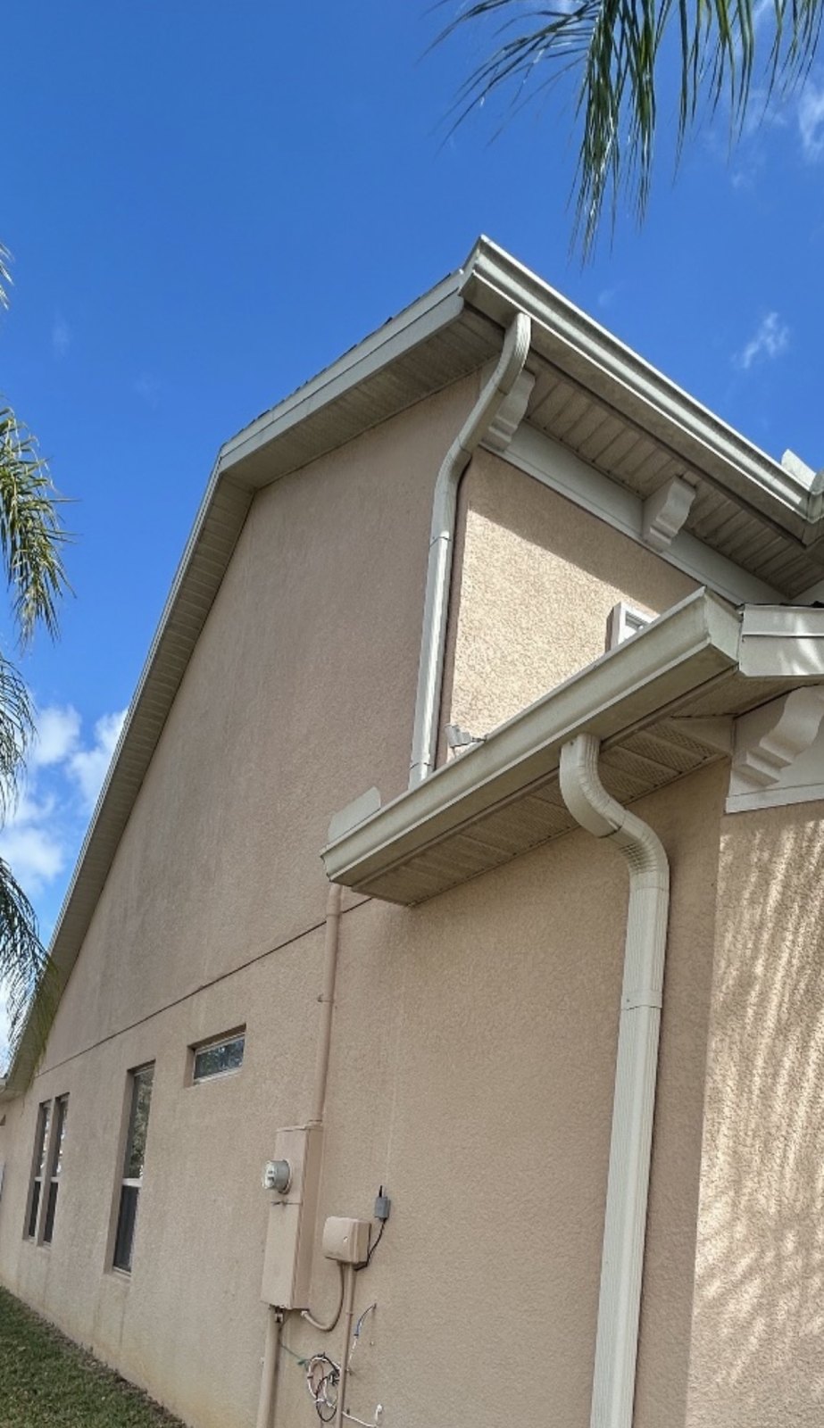 Finished: two-story stucco house with freshly painted white fascia, soffits, gutters and downspouts